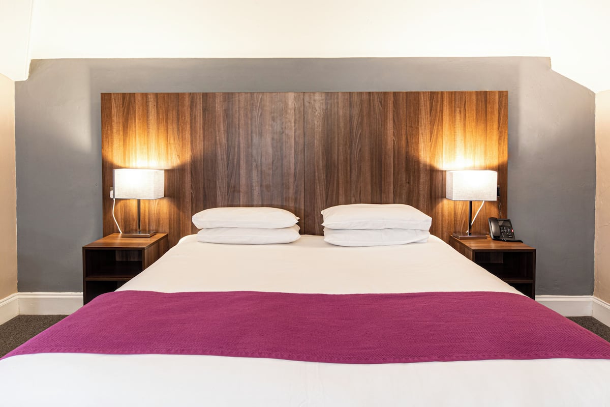 Una habitación de hotel con una cama grande, dos mesitas de noche con lámparas y un cabecero de madera.