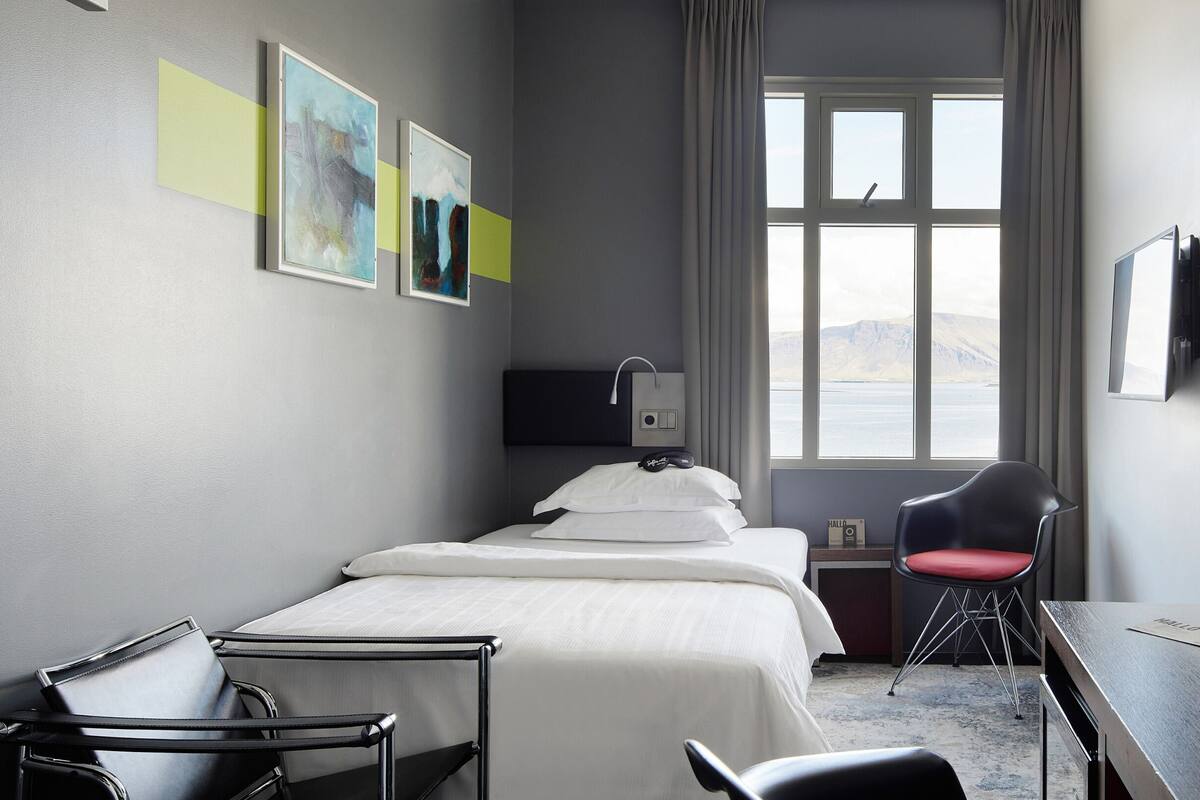 Een hotelkamer met een bed, een bureau, een stoel, een televisie en een raam met uitzicht.