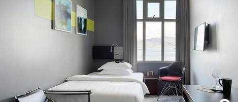 Ein Hotelzimmer mit Bett, Schreibtisch, Stuhl, Fernseher und einem Fenster mit Aussicht.