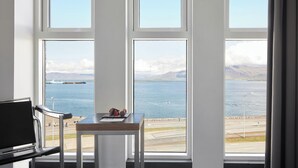 Una habitación con ventanas amplias que dan a un cuerpo de agua, un muelle y montañas distantes.