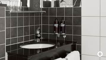 Un baño con un lavamanos negro, un espejo y dos botellas de crema corporal y jabón de manos.