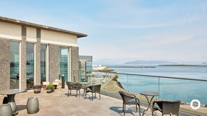 Una terraza con asientos al aire libre, vistas al mar y un edificio con grandes ventanales.