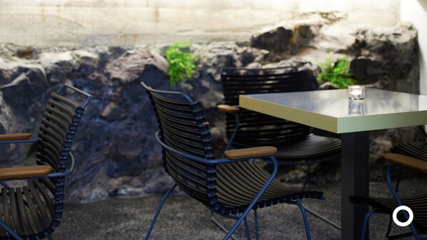 Un comedor con sillas de metal y una mesa, un muro de piedra y una planta pequeña.