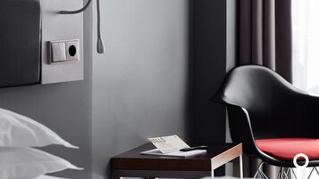 Habitación de hotel moderna con diseño minimalista, que incluye un escritorio con bloc de notas y bolígrafo, una silla negra con cojín rojo y un teléfono montado en la pared.