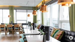 Een moderne eetruimte met een lange tafel, stoelen en een zwarte leren bank met kussens.