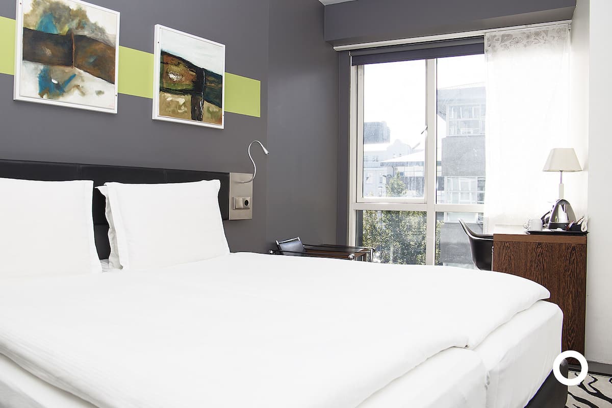 Een hotelkamer met een groot bed, een bureau met lamp en twee schilderijen aan de muur.