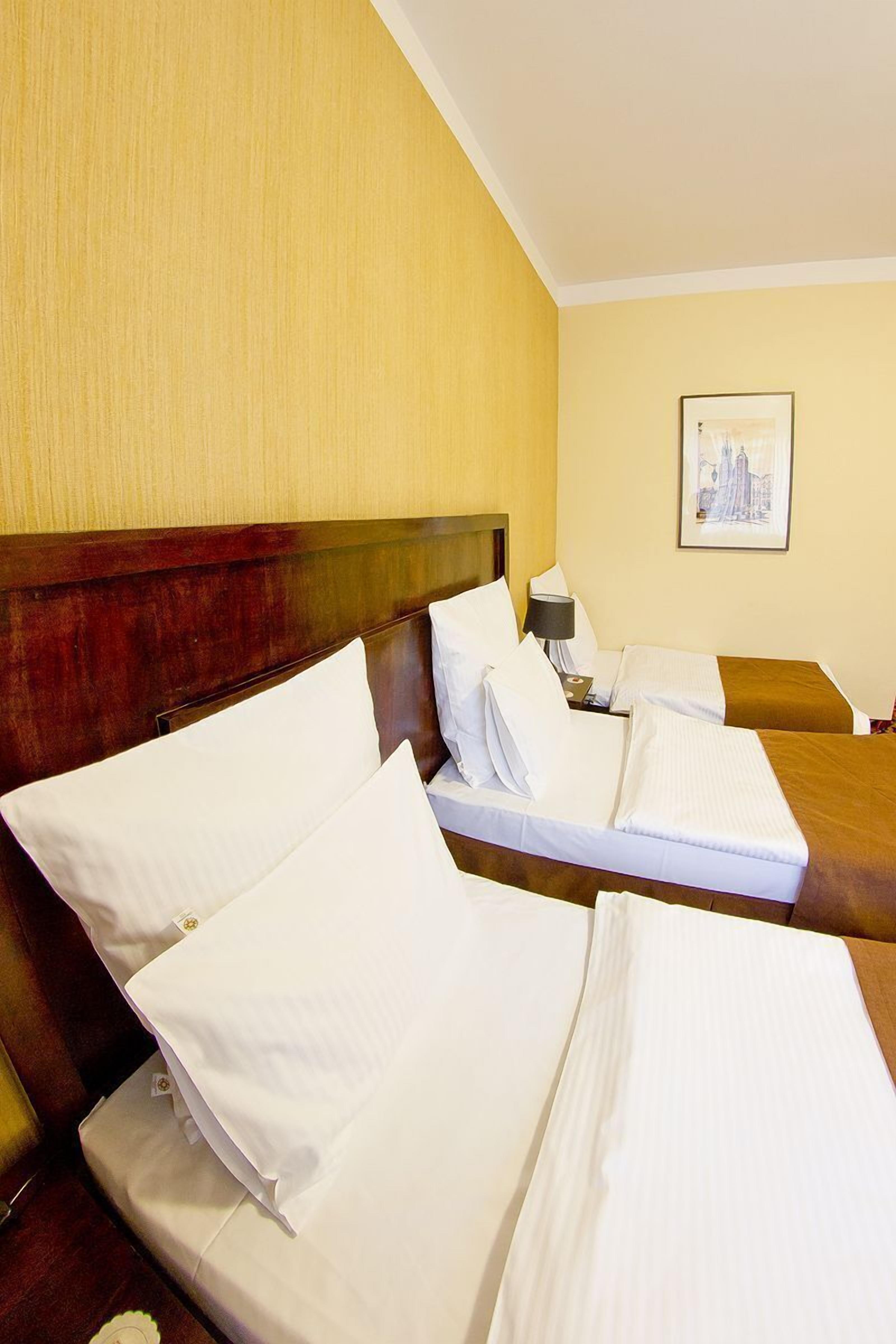 Ein Hotelzimmer mit zwei Betten, einem Holz-Kopfteil, einem Nachttisch mit Lampe und einem gerahmten Bild an der Wand.