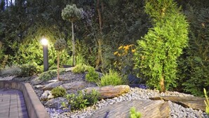 A landscaped garden with a paved walkway, large rocks, and various shrubs and trees. - Columbus Hotel (Kraków)