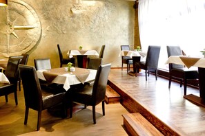 A restaurant with wooden flooring, tables with white tablecloths, and dark leather chairs. - Columbus Hotel (Kraków)