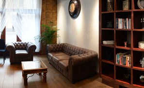 A living room with a brown leather sofa, two armchairs, a wooden coffee table, a bookshelf, and a wall clock. - Columbus Hotel (Kraków)