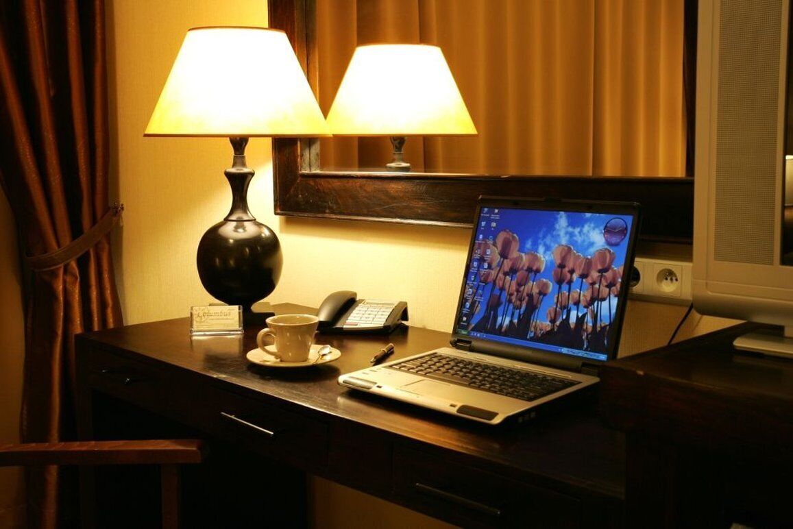 Une chambre d’hôtel équipée d’un bureau, d’un ordinateur portable, d’un téléphone, d’une tasse et de deux lampes.