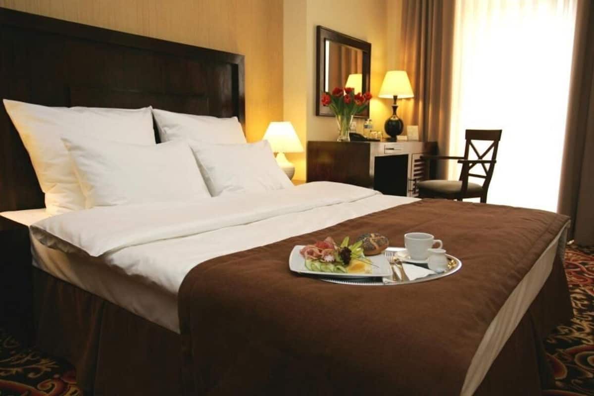A hotel room with a neatly made bed, a breakfast tray with food and drinks, a desk with a lamp, and a chair.