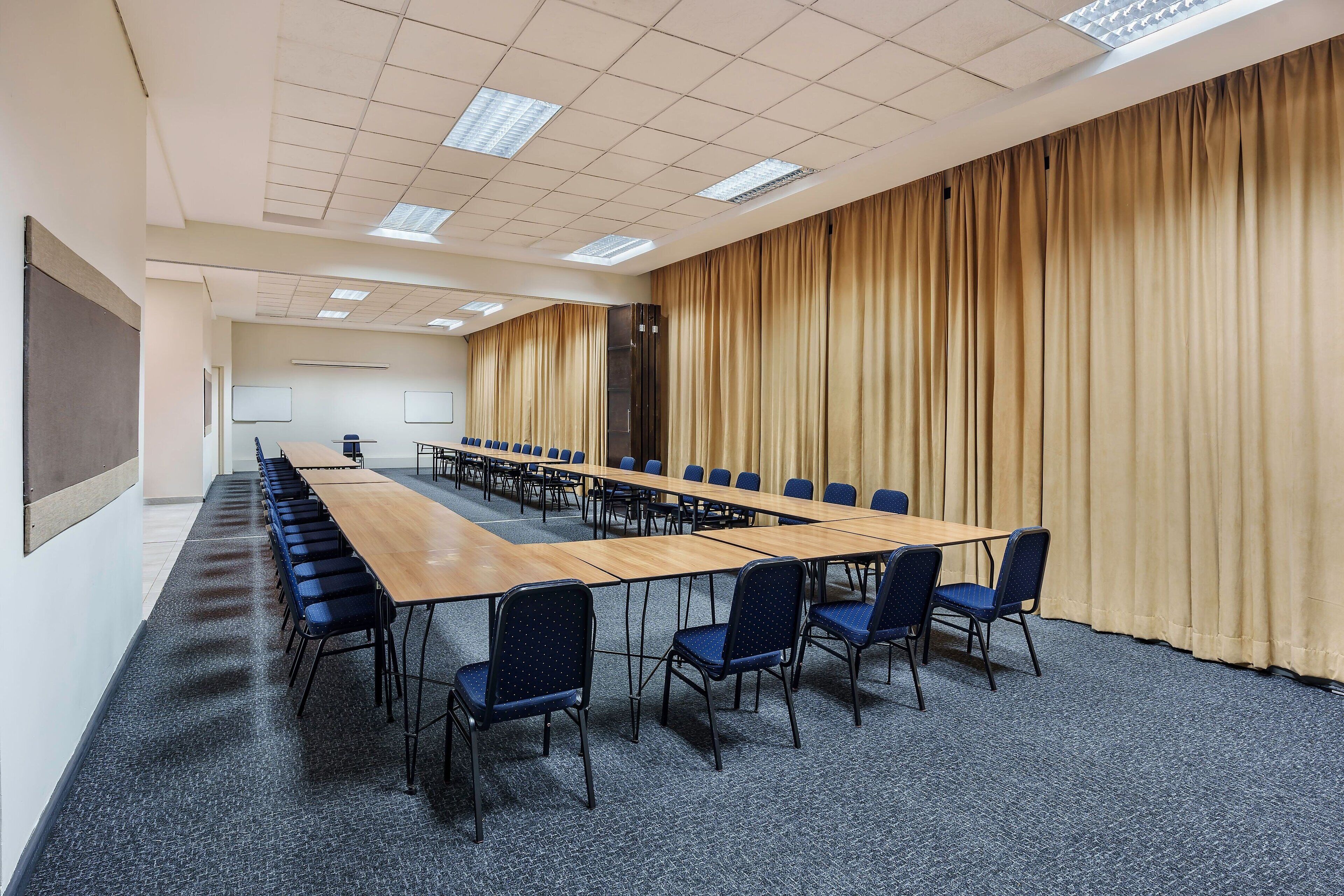 A conference room with a long table, blue chairs, a projector screen, and a large curtain.