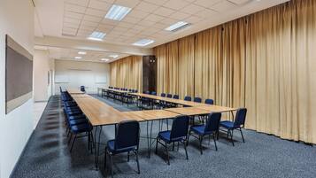 A conference room with a long table, blue chairs, a projector screen, and a large curtain.