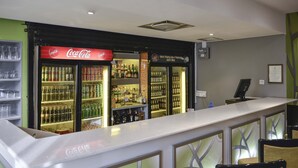 Un espace bar avec un réfrigérateur Coca-Cola, des étagères remplies de bouteilles et un comptoir où est affiché le menu.