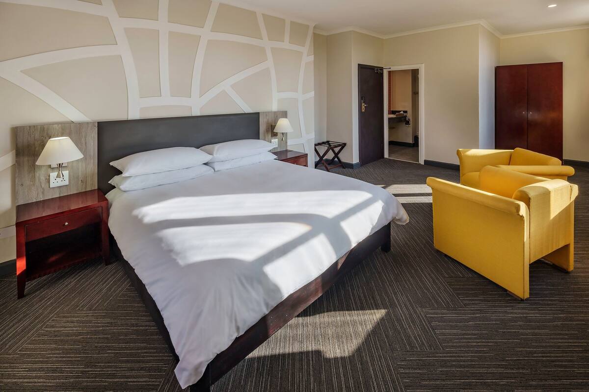 Une chambre d’hôtel avec un grand lit, une table de chevet avec une lampe, une chaise et une armoire.