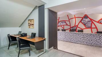A modern office space with a reception desk, two desks with computers, and black chairs.