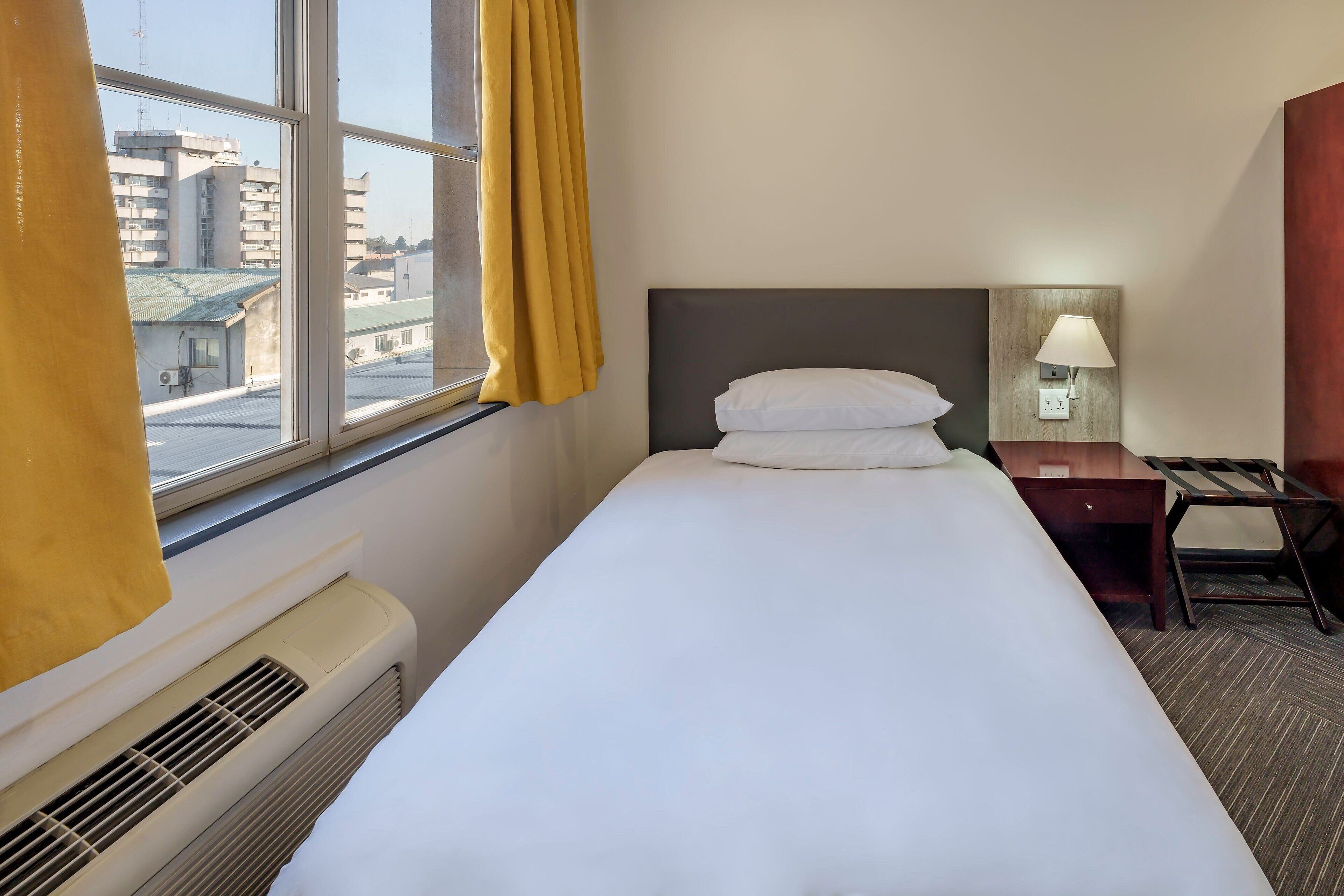 Una habitación de hotel con cama, escritorio, lámpara y ventana con cortinas.