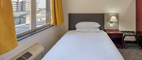 A hotel room with a bed, a desk, a lamp, and a window with curtains.