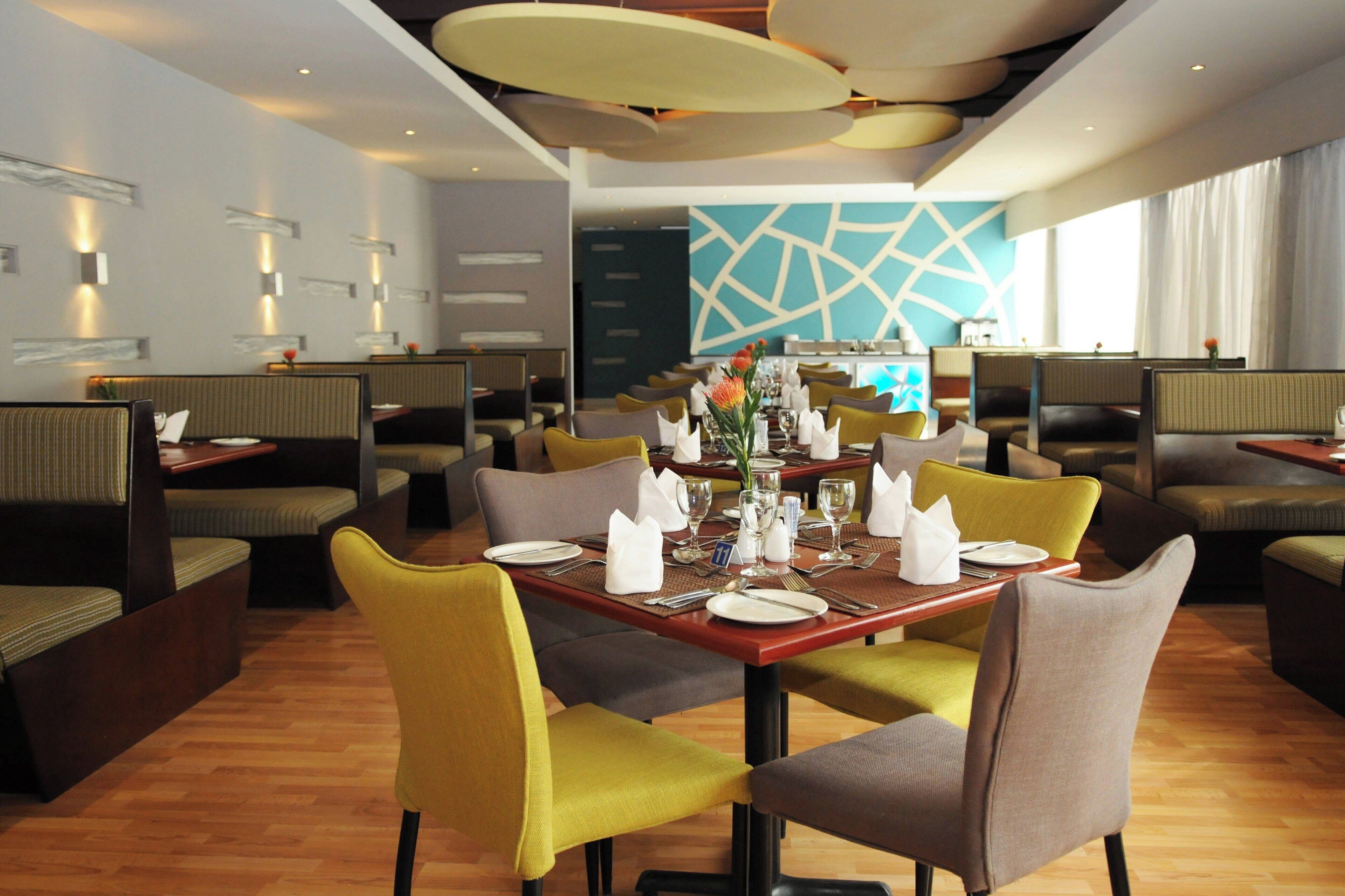 A modern restaurant with booth seating, a central dining table set with white tableware, and a geometric wall design.