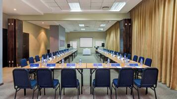 A conference room with a long table, chairs, water bottles, nameplates, and a projector screen.