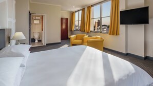 Une chambre d’hôtel avec un grand lit, un téléviseur fixé au mur, une fenêtre avec des rideaux et une vue sur la ville.