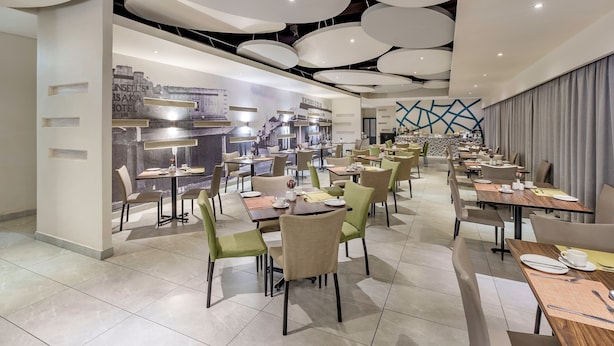Un espace de restauration moderne doté de plusieurs tables et chaises, d’un bar central et d’un mur orné d’une fresque représentant un paysage urbain.