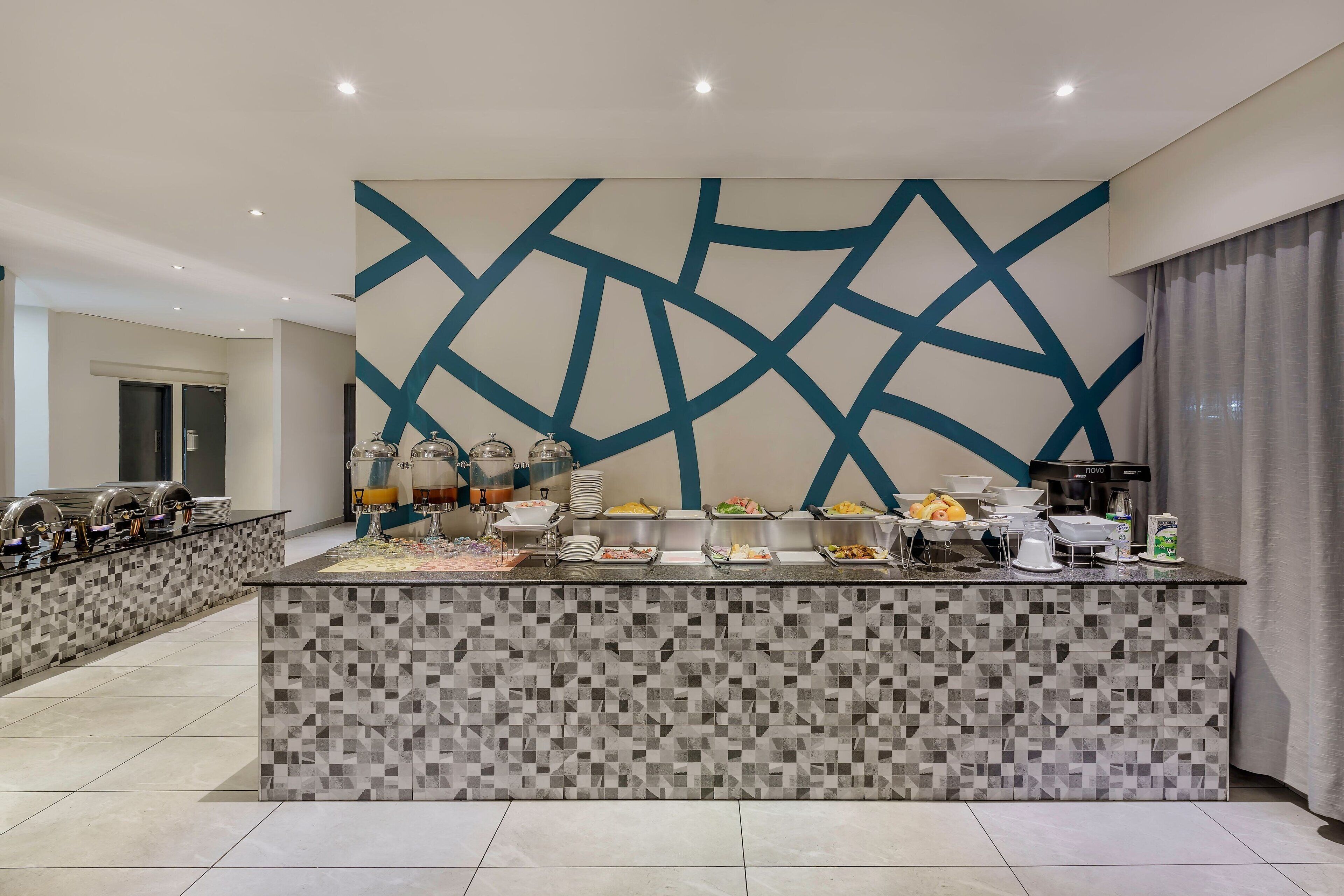A modern hotel lobby with a buffet area featuring a geometric wall design and a tiled floor.