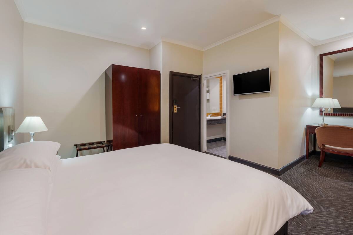 Une chambre d’hôtel avec un grand lit, un bureau avec une chaise, un téléviseur fixé au mur et une armoire.