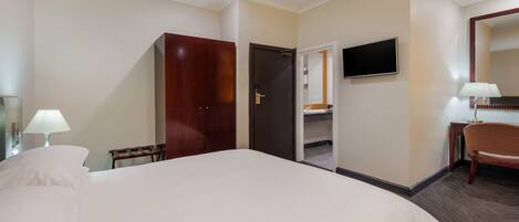A hotel room with a large bed, a desk with a chair, a TV mounted on the wall, and a wardrobe.