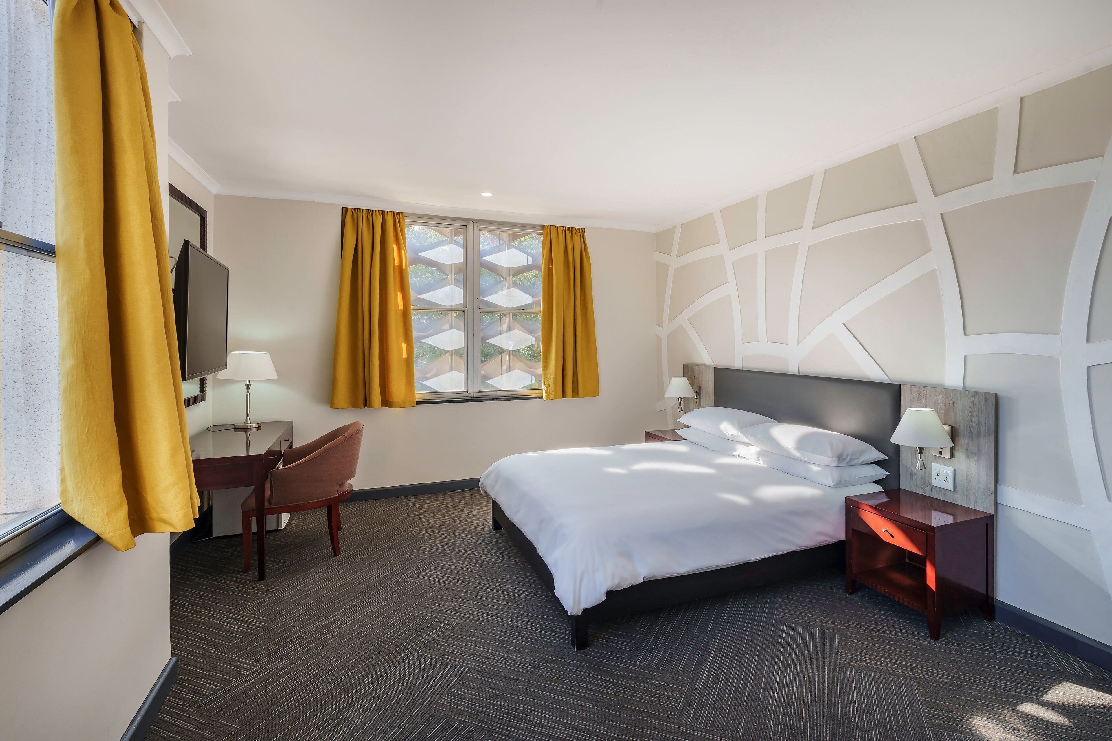 A hotel room with a bed, a desk, a chair, a TV, and a window with curtains.