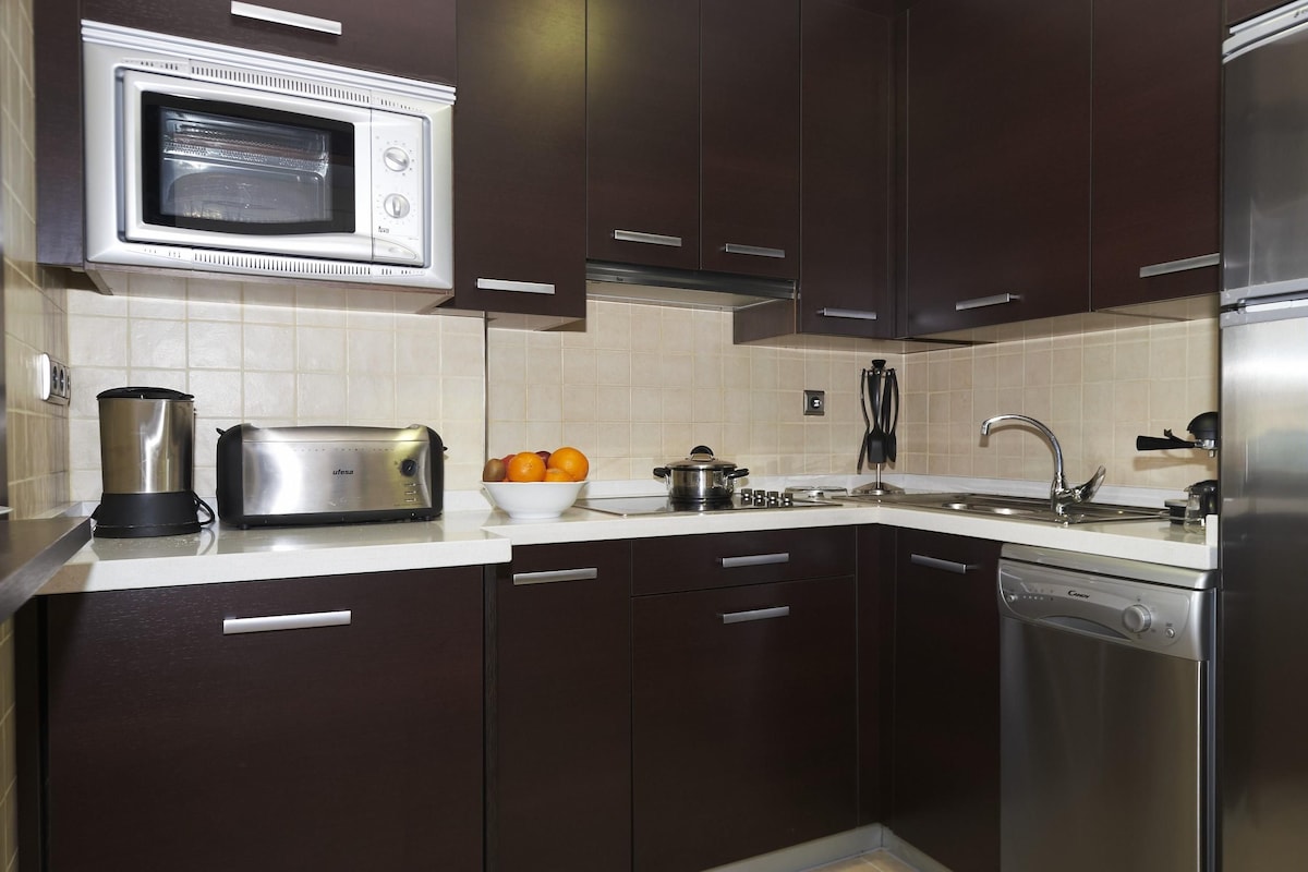 Une cuisine moderne avec des meubles de couleur sombre, un four à micro-ondes, un grille-pain, un évier et un lave-vaisselle.