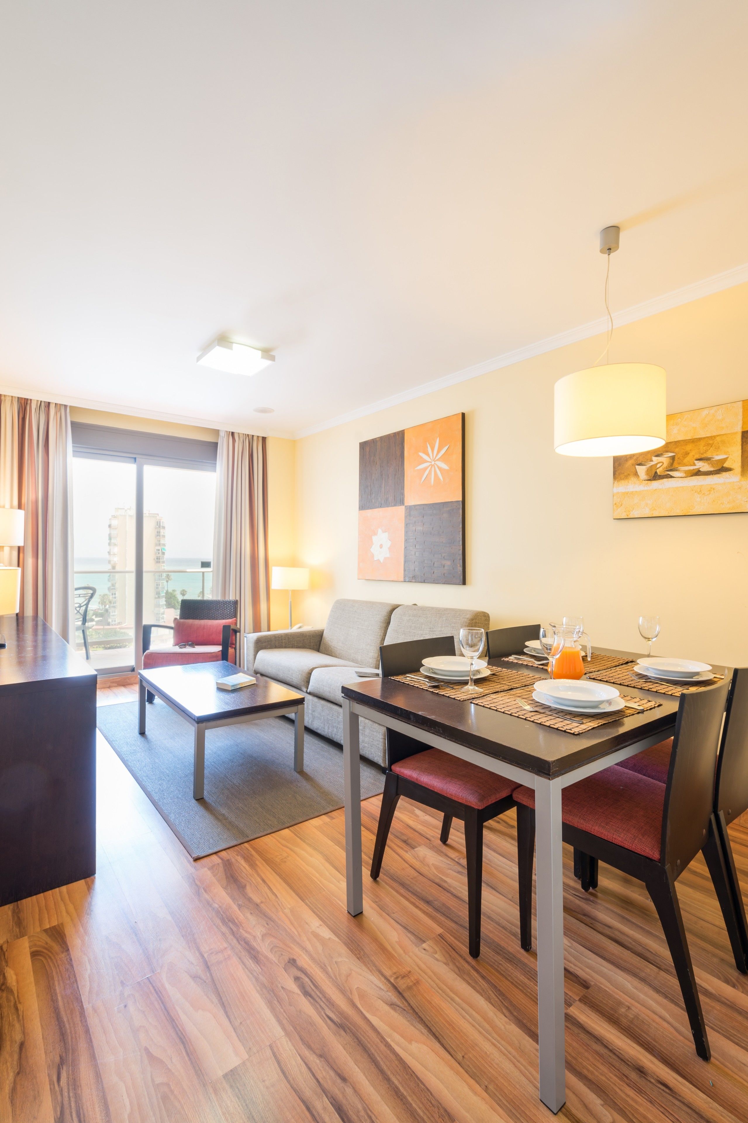 Habitación de hotel moderna con comedor, sofá, mesa de centro y vistas a la ciudad.