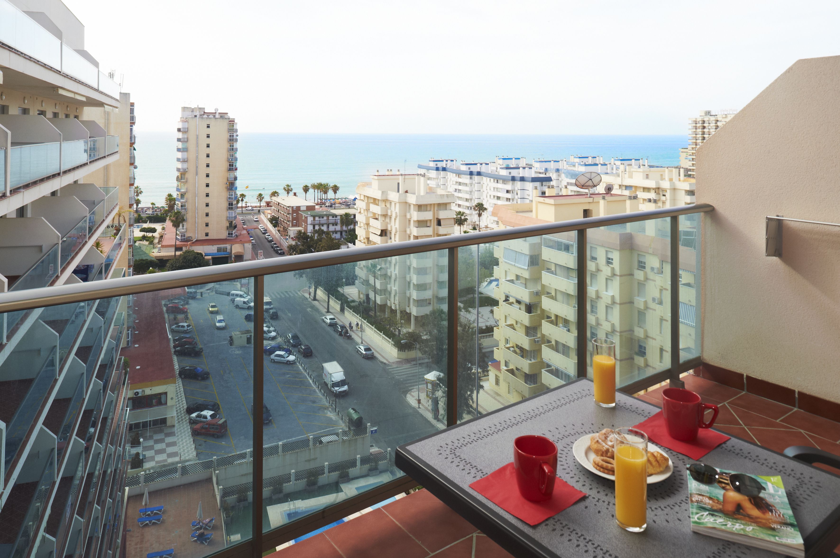 Ein Balkon mit einem Frühstückstisch, mit Blick auf eine Stadtlandschaft und das Meer.