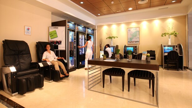 Un espace d’accueil d’hôtel comprenant des fauteuils de massage, un comptoir d’accueil et un poste informatique.