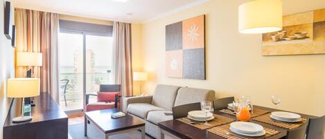 A hotel room with a dining area, a sofa, a table with plates and glasses, and a view of the city.