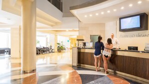 Un espace d’accueil d’hôtel comprenant un comptoir d’enregistrement, un téléviseur fixé au mur et un aménagement intérieur moderne.