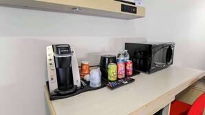 A kitchenette with a Keurig coffee maker, a microwave, a remote control, and various beverages. - Signature Inn Berkeley (Berkeley)