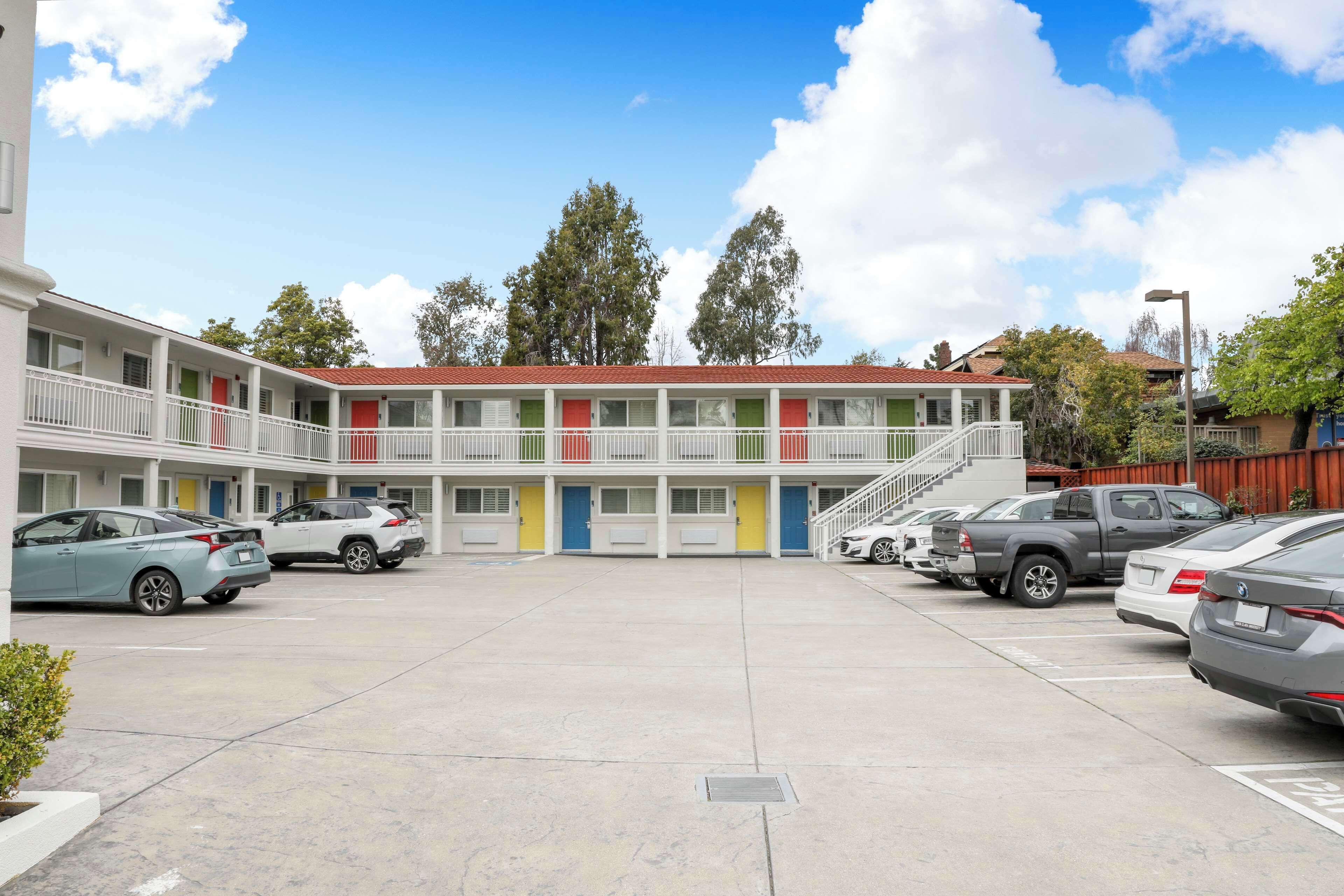 A motel with a parking lot, multiple units with balconies, and a red-tiled roof.