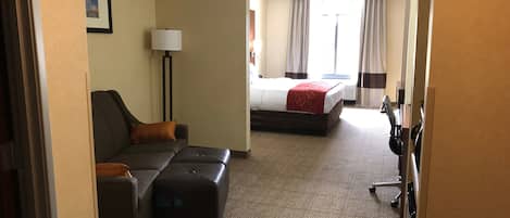 Una habitación de hotel con sofá, reposapiés y cama con manta roja.