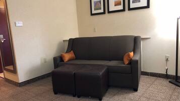 A dark brown leather sofa with two orange cushions, a matching ottoman, and three framed pictures on the wall.