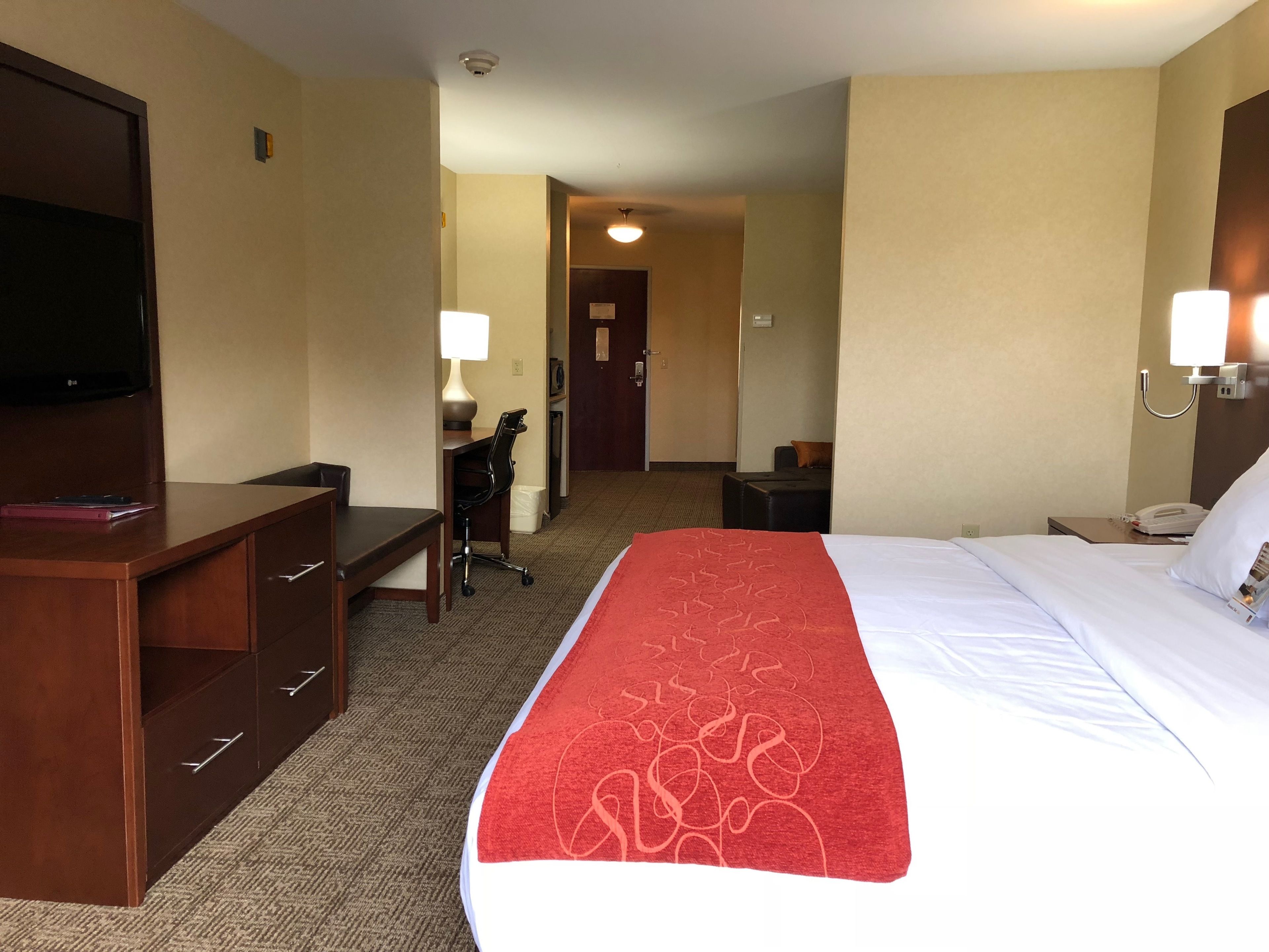 A hotel room with a bed, a desk, a chair, a TV, and a lamp.