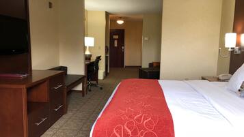 A hotel room with a bed, a desk, a chair, a TV, and a lamp.