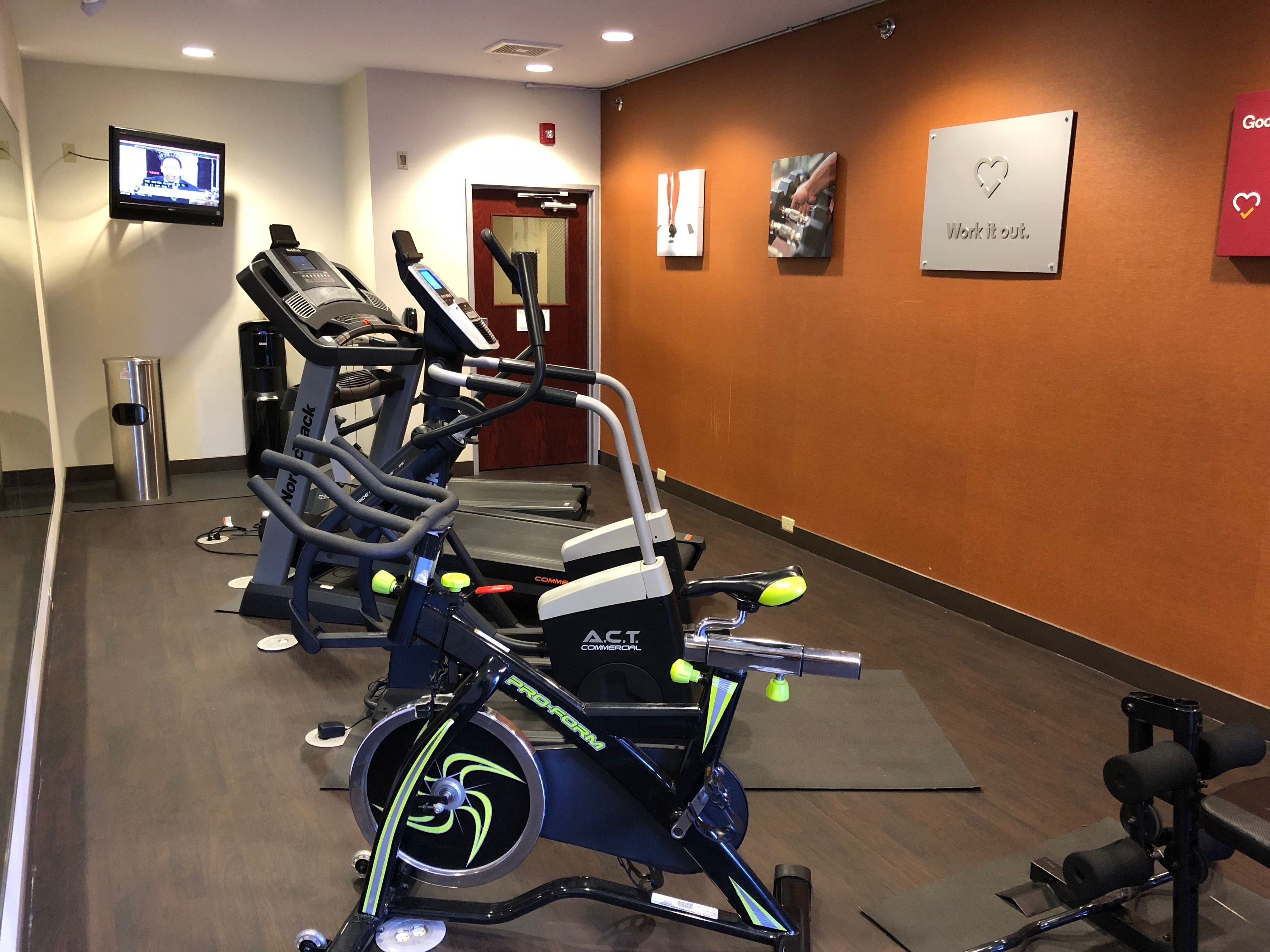 Een sportschool met cardioapparaten, een televisie en motiverende posters aan de muur.