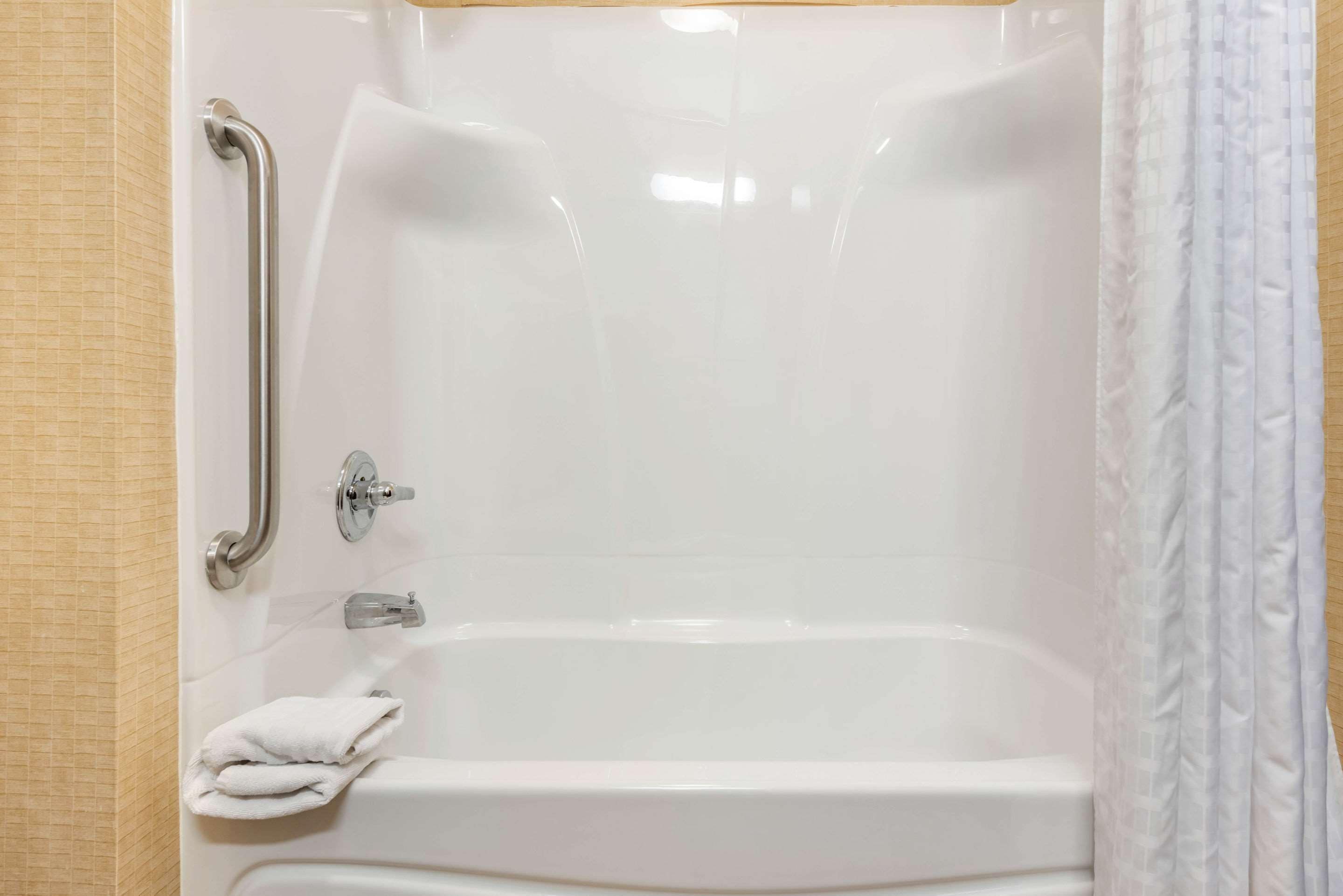 A white bathtub with a grab bar, a towel rack, and a shower curtain.