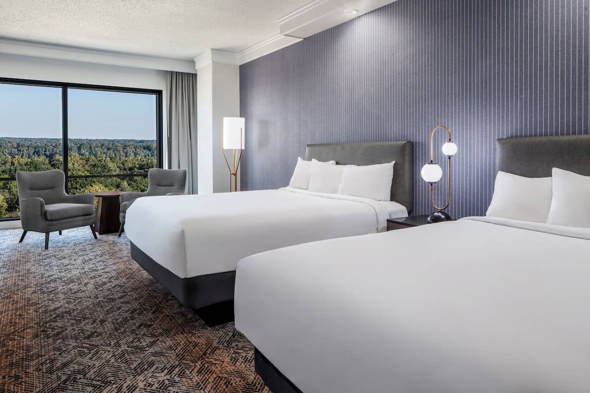 A hotel room with two beds, a view of the forest, and a large window.