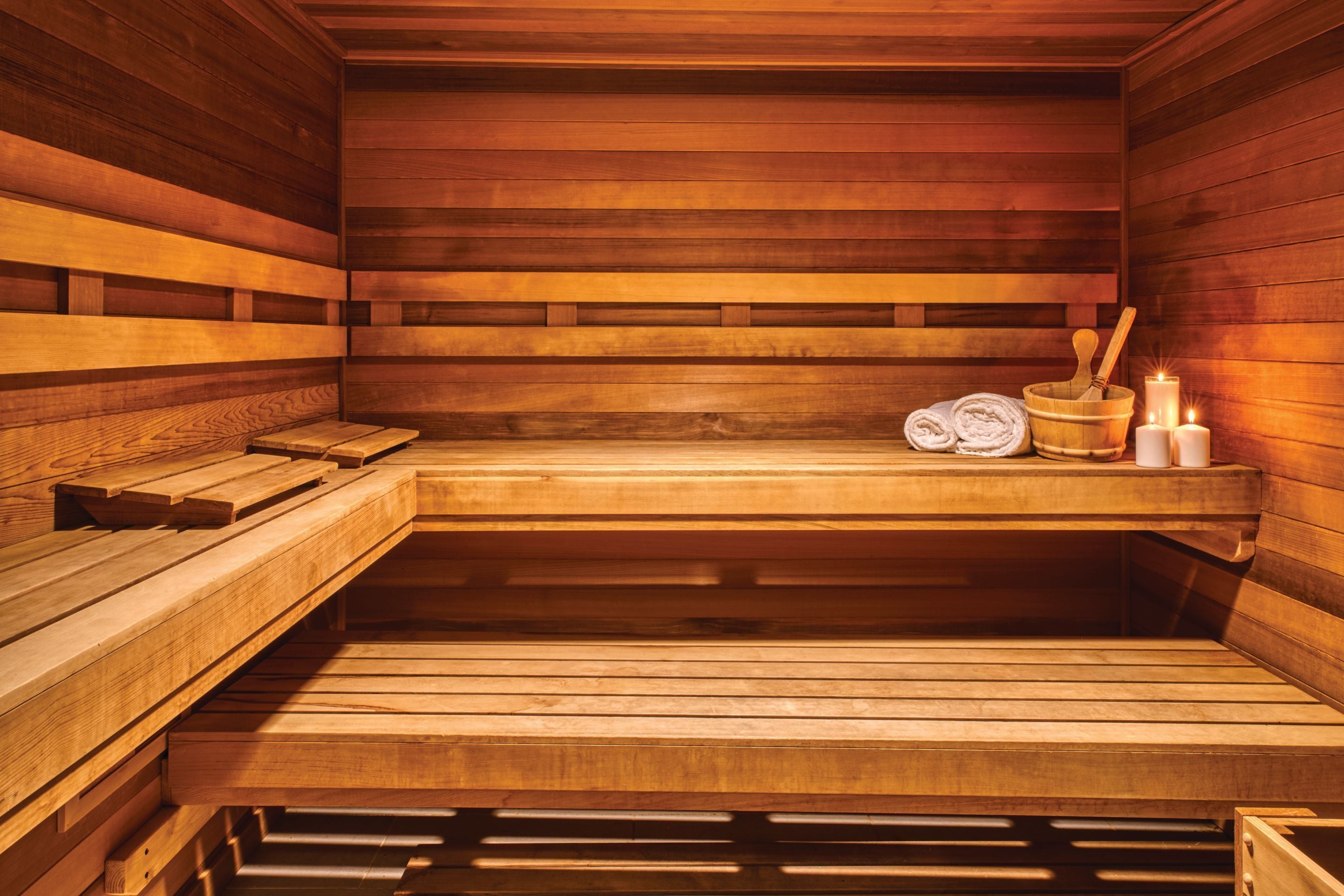 A wooden sauna with benches, a bucket, candles, and towels.