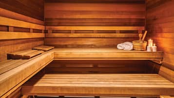 A wooden sauna with benches, a bucket, candles, and towels.