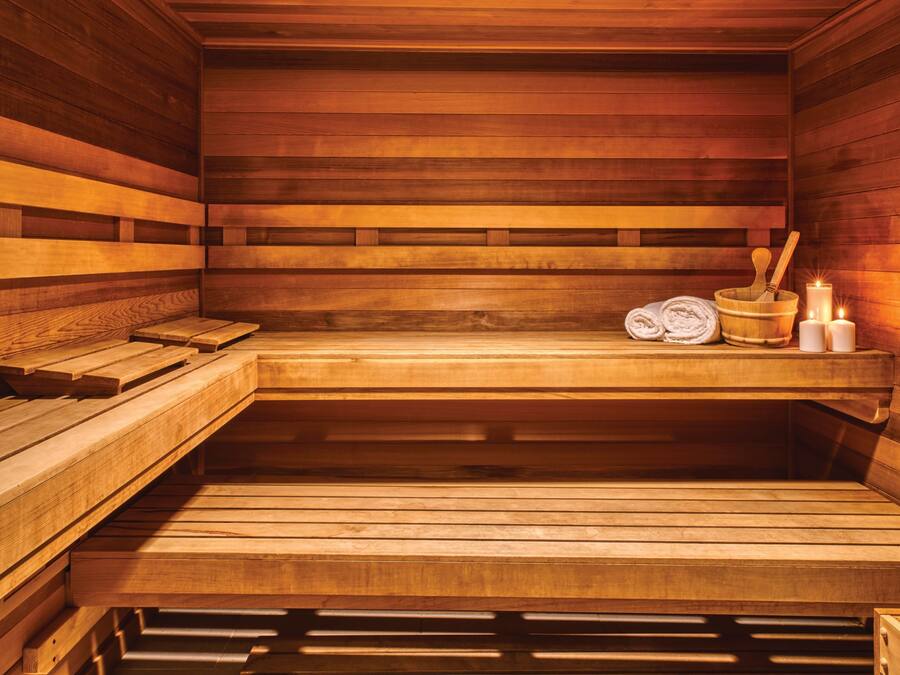 A wooden sauna with benches, a bucket, candles, and towels.