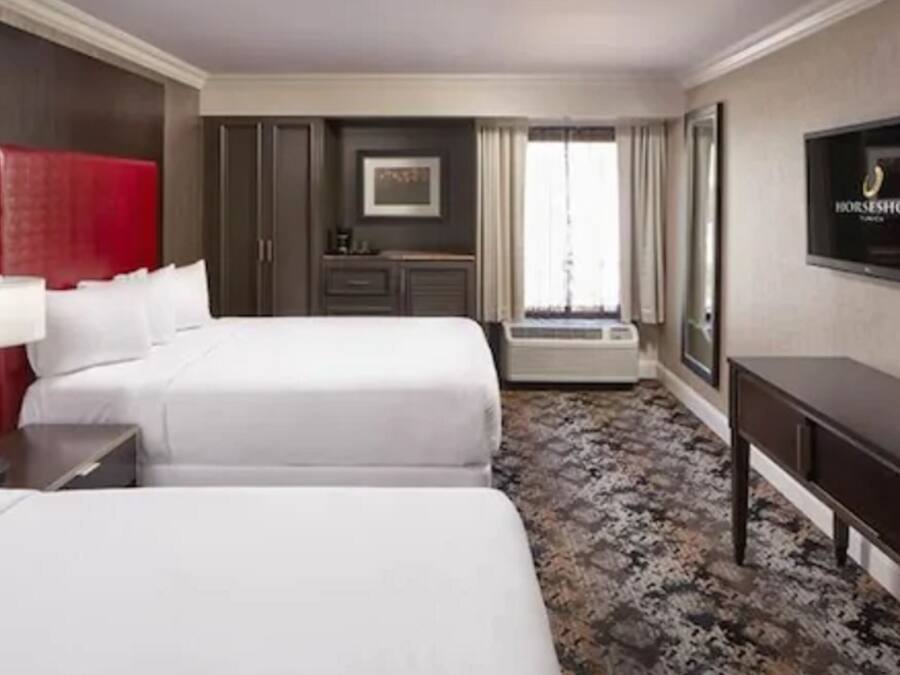 Camera d'albergo con due letti, un poggiatesta rosso, una televisione, una scrivania e un armadio.